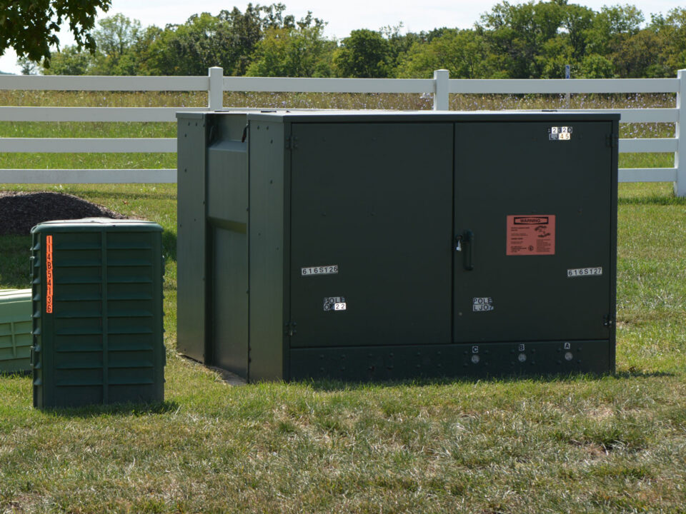Pad-mounted power and communications enclosures beside a white fence
